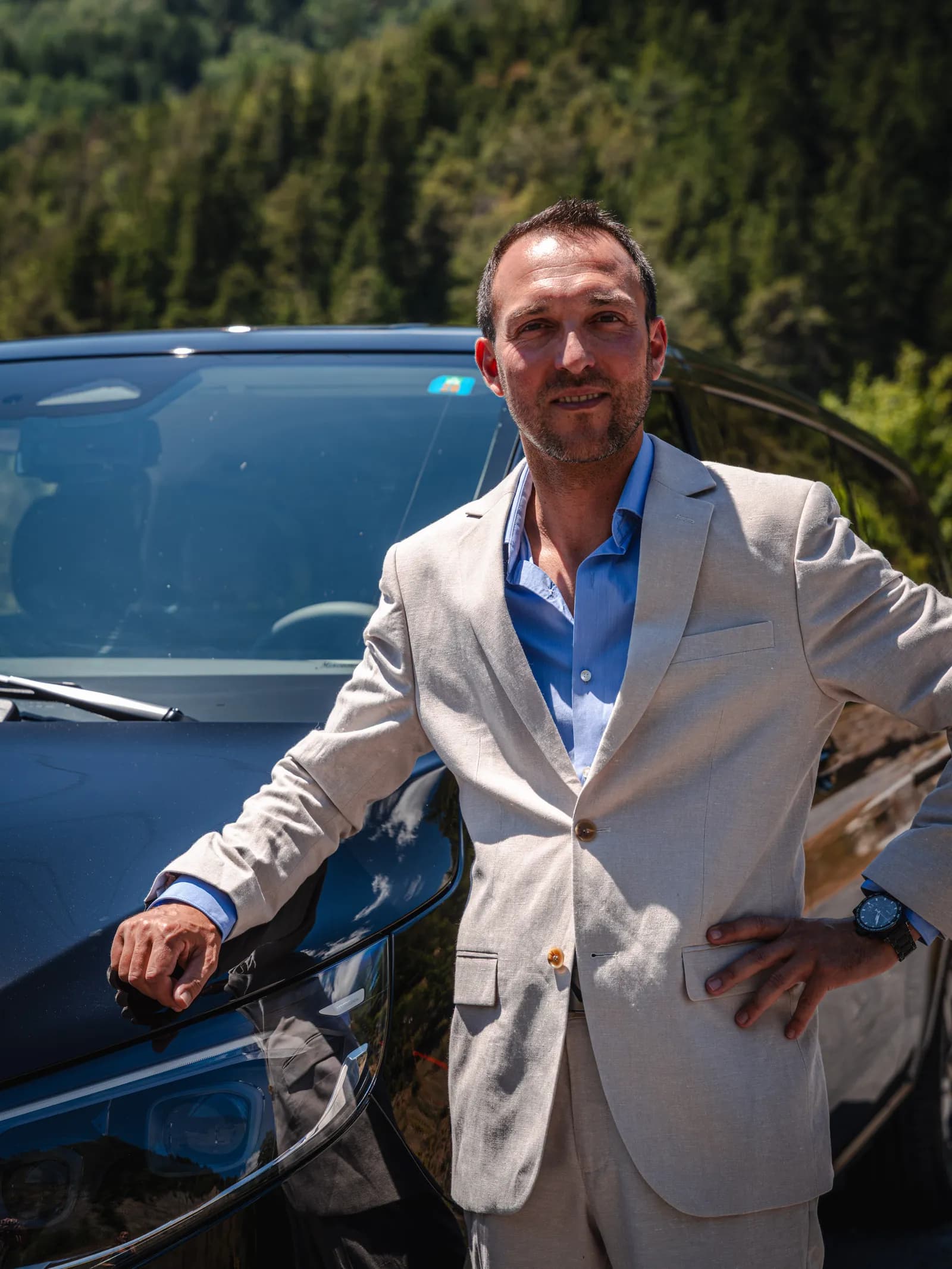 Julien Duret, fondateur d'All in Taxi, en costume devant son van Mercedes à Crans-Montana